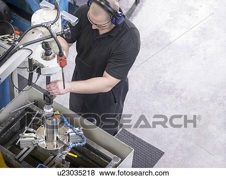 Stock Photo - Worker drilling steel rod in factory. Fotosearch