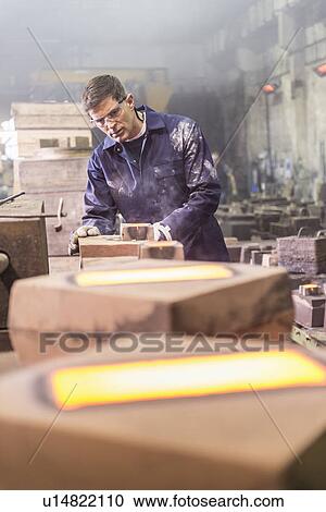 Stock Image - Worker examining moulds in metal foundry. Fotosearch