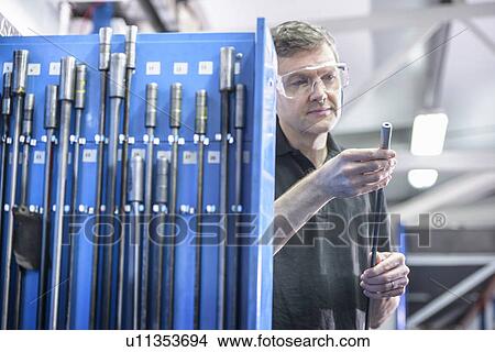 Worker inspecting drill rods in factory View Large Photo Image Picture - Worker inspecting drill rods in factory. Fotosearch