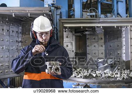 Stock Photo - Worker inspecting metal in foundry. Fotosearch