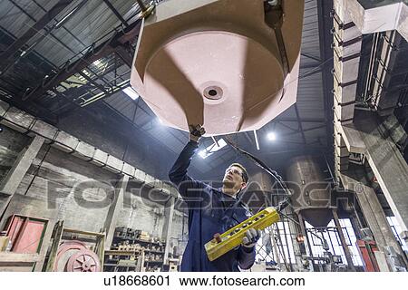 Stock Image - Worker inspecting mould in foundry. Fotosearch