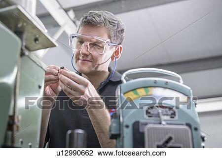 Stock Image - Worker polishing steel parts in factory. Fotosearch
