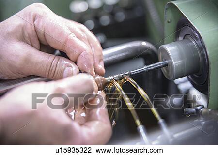 Stock Image - Worker polishing steel parts in factory. Fotosearch
