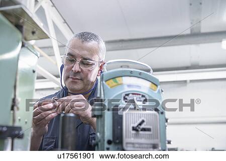Stock Image - Worker polishing steel parts in factory. Fotosearch