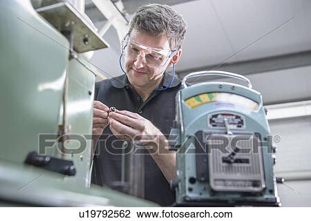 Stock Image - Worker polishing steel parts in factory. Fotosearch