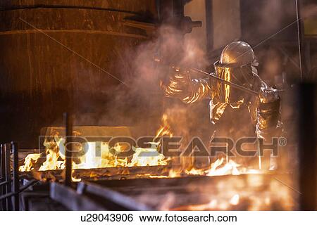 Stock Photograph - Worker pouring molten metal in factory. Fotosearch