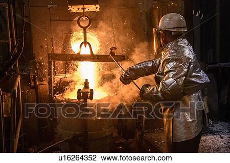 Stock Image - Worker pouring molten metal in foundry. Fotosearch