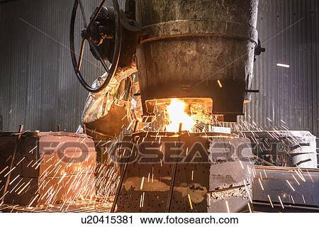 Stock Image - Worker pouring molten metal in foundry. Fotosearch