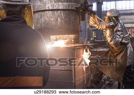 Stock Image - Worker pouring molten metal in foundry. Fotosearch