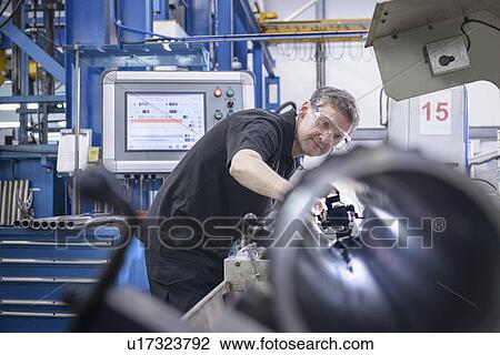 Stock Image - Worker using machinery in factory. Fotosearch