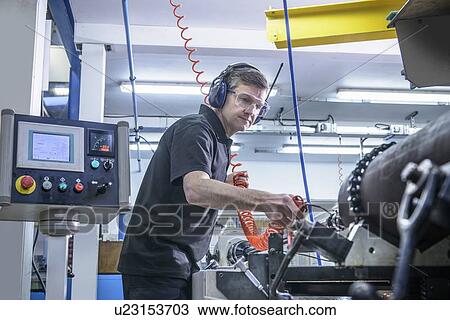 Stock Image - Worker using machinery in factory. Fotosearch
