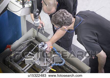 Stock Image - Workers examining steel rod in factory. Fotosearch
