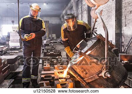 Stock Photo - Workers pouring molten metal in foundry. Fotosearch