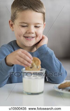 Stock Photography - Boy (4-5) dipping cookie in milk. Fotosearch