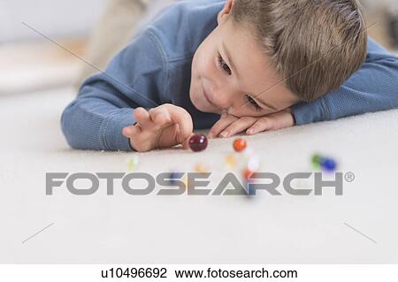 Stock Image - Boy (4-5) playing with marbles. Fotosearch