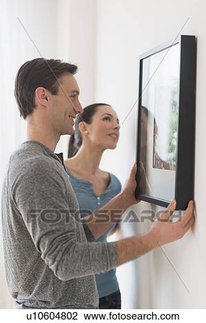 Stock Image - Couple hanging picture on wall. Fotosearch