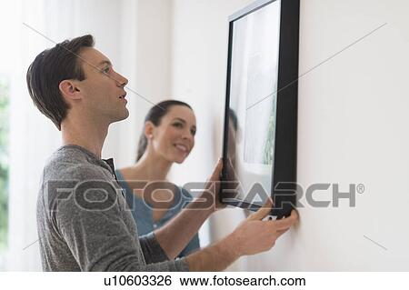 Stock Photograph - Couple hanging picture on wall. Fotosearch