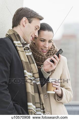Couple in winter clothes looking at phone View Large Photo Image Stock Photo - Couple in winter clothes looking at phone. Fotosearch