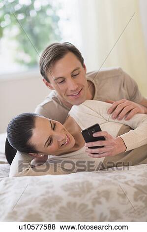 Couple lying on bed and looking at phone View Large Photo Image Stock Photo - Couple lying on bed and looking at phone. Fotosearch