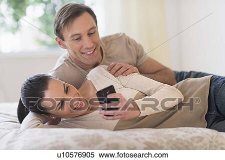 Couple lying on bed and looking at phone View Large Photo Image Stock Photography - Couple lying on bed and looking at phone. Fotosearch