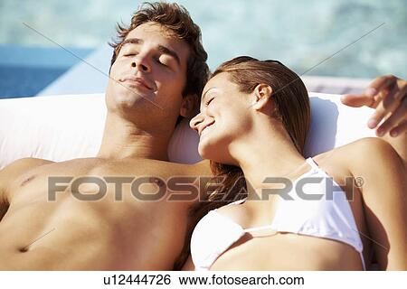 Stock Photograph - Couple sunbathing at swimming pool. Fotosearch