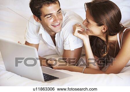 Stock Photograph - Couple using laptop while lying in bed. Fotosearch