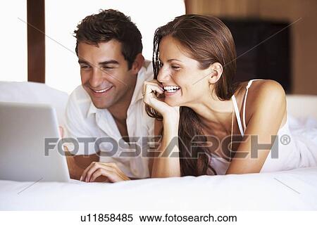 Stock Photography - Couple using laptop while lying in bed. Fotosearch