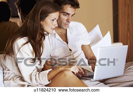 Couple using laptop while sitting on bed View Large Photo Image Stock Image - Couple using laptop while sitting on bed. Fotosearch