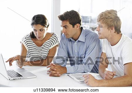 Picture - Coworkers at table looking at laptop. Fotosearch