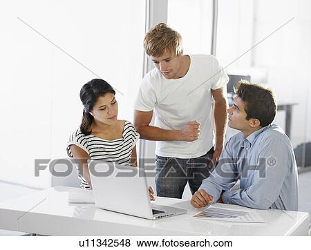 Coworkers talking at table, using laptop View Large Photo Image Stock Photo - Coworkers talking at table, using laptop. Fotosearch