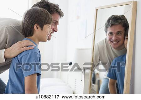 Stock Photo - Father and son (8-9) looking into mirror. Fotosearch
