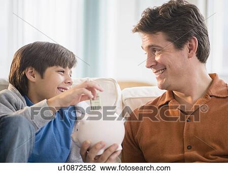 Stock Image - Father and son (8-9) putting money into piggybank. Fotosearch