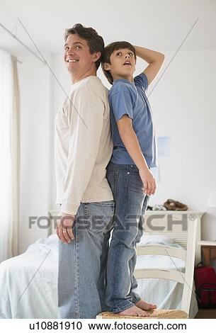 Stock Image - Father and son (8-9) standing back to back. Fotosearch