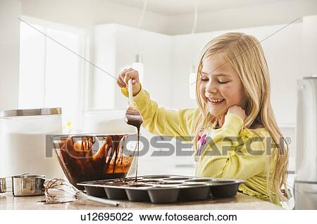 Stock Image - Girl (6-7) baking cupcakes. Fotosearch