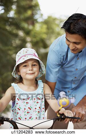 Man assisting girl (6-7) riding bicycle View Large Photo Image Stock Image - Man assisting girl (6-7) riding bicycle. Fotosearch