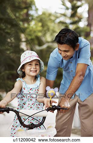 Stock Image - Man assisting girl (6-7) riding bicycle. Fotosearch