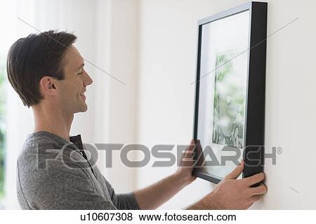 Stock Photo - Man hanging picture on wall. Fotosearch
