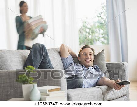 Stock Photo - Man lying on sofa watching tv. Fotosearch