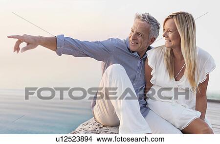 Picture - Mature couple sitting by seashore. Fotosearch