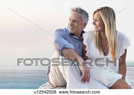 Stock Photo - Mature couple sitting by seashore. Fotosearch