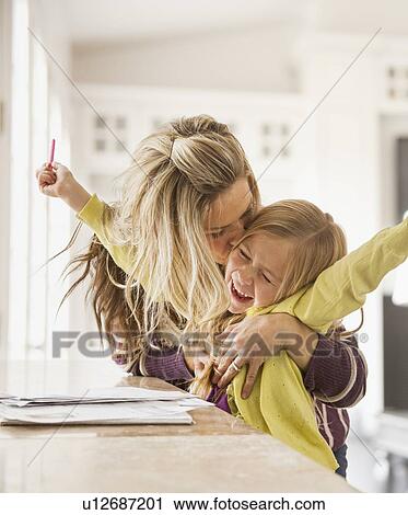 Stock Image - Mother kissing daughter (6-7) during doing homework. Fotosearch