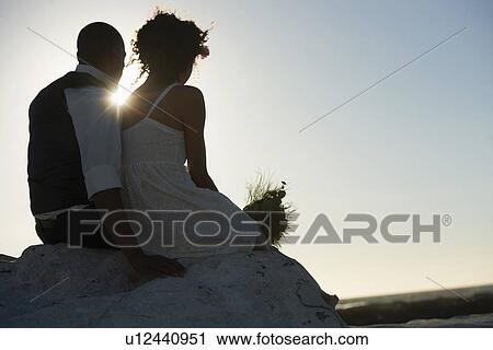 Stock Image - Newlywed couple looking at setting sun. Fotosearch