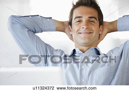 Stock Image - Portrait of man relaxing, hands behind head. Fotosearch