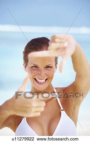 Stock Image - Portrait of woman looking through finger frame. Fotosearch