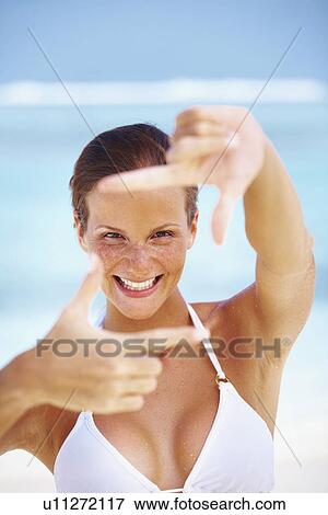 Stock Photo - Portrait of woman looking through finger frame. Fotosearch