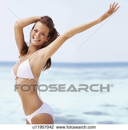 Stock Image - Portrait of young woman in bikini, arms raised. Fotosearch