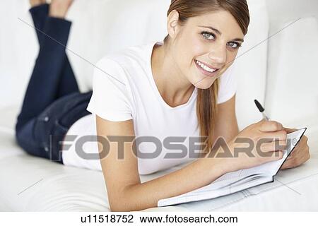Stock Image - Portrait of young woman writing in notepad. Fotosearch