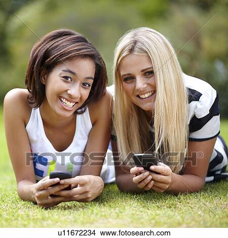 Portrait of young women lying on grass, using mobile phone View Large Photo Image Picture - Portrait of young women lying on grass, using mobile phone. Fotosearch