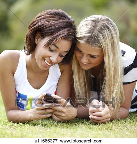 Portrait of young women lying on grass, using mobile phone View Large Photo Image Stock Photo - Portrait of young women lying on grass, using mobile phone. Fotosearch
