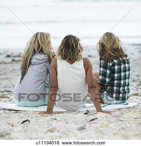 Stock Photo - Rear view of people sitting on beach. Fotosearch